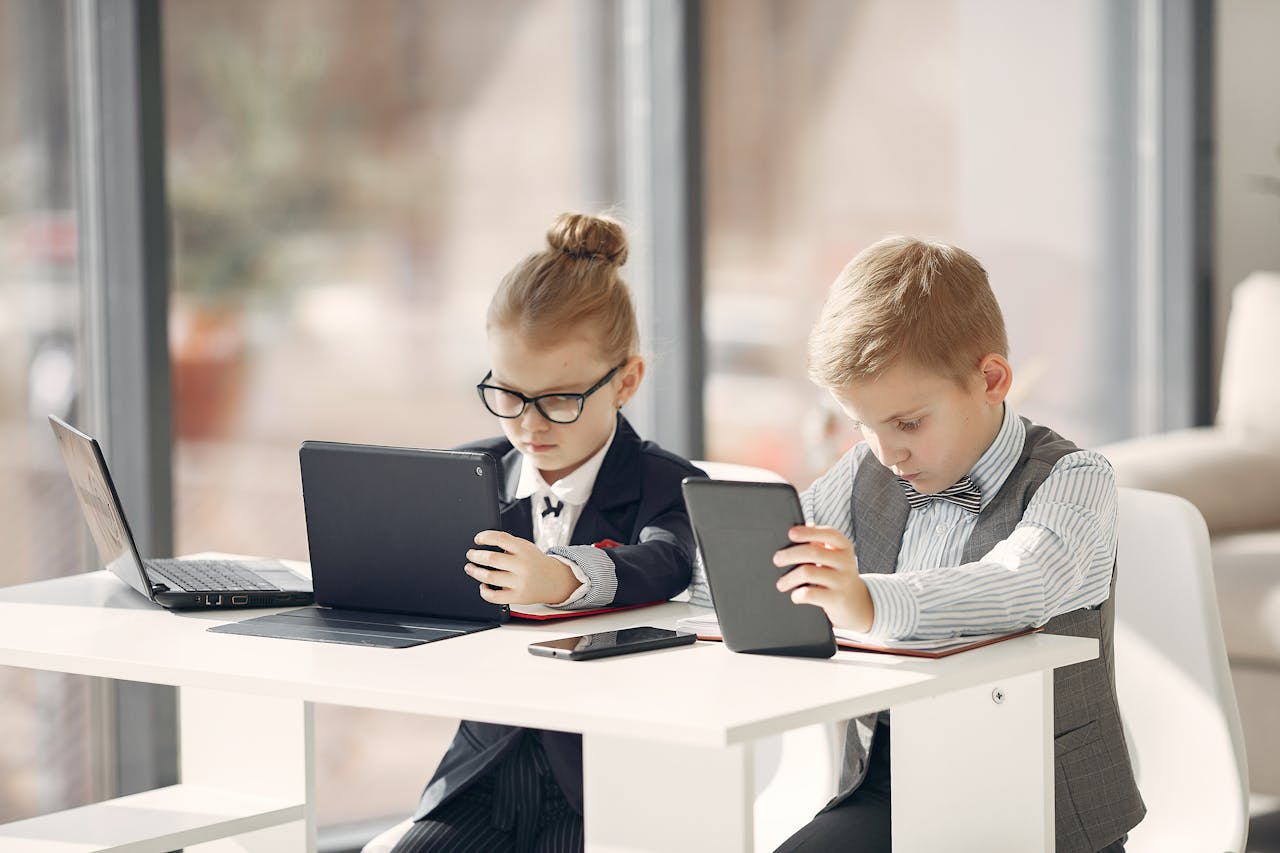 hero-img-02 Adorable kids in formal wear working on gadgets together while sitting at table in light workplace at daytime