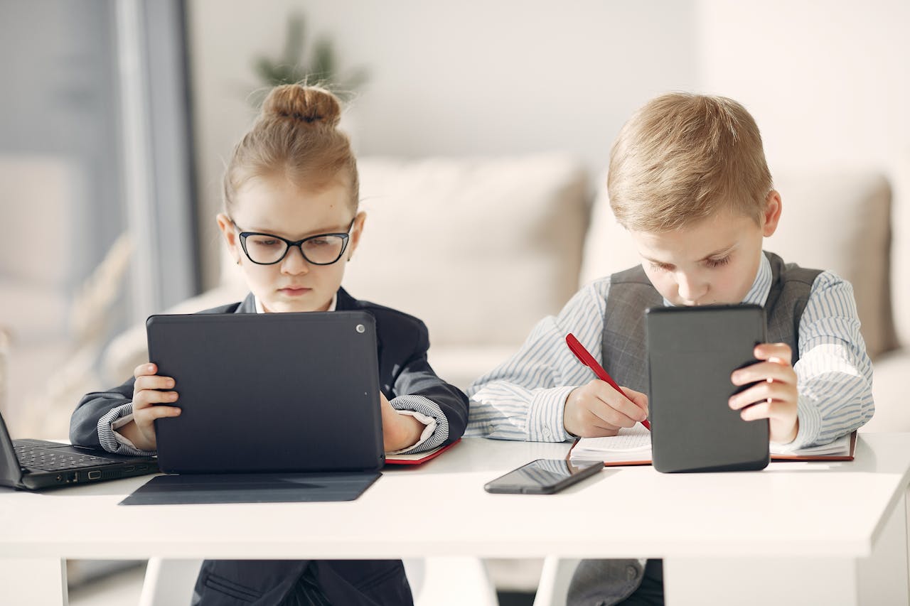 services-02 Smart business children wearing formal clothes and eyeglasses surfing tablets and writing notes in daily planner in modern office