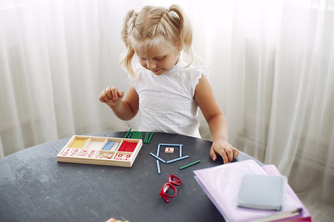gallery-3 Blond little girl standing while playing with puzzle in living room at home and counting sticks different colors during weekend