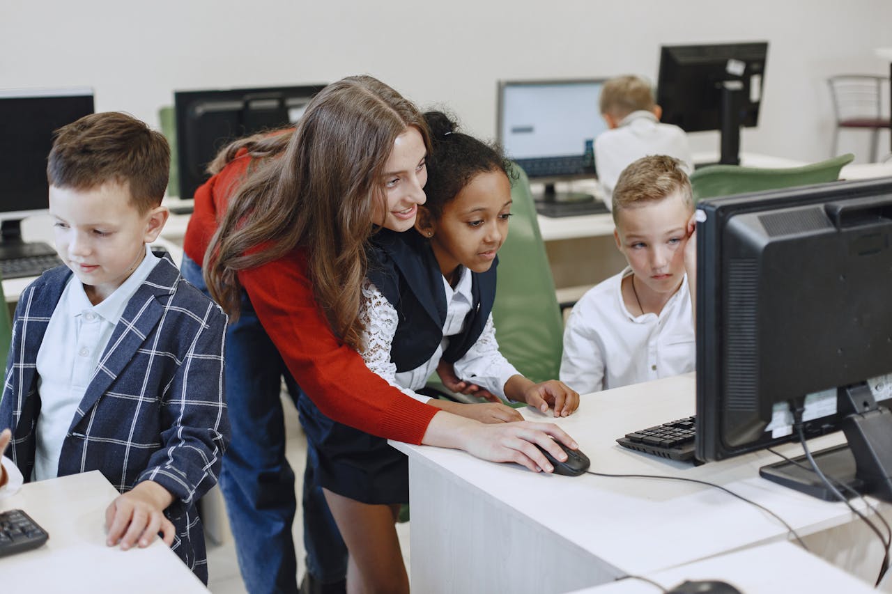 services-02 Teacher engaging with diverse children in a technology lesson using computers in a modern classroom.